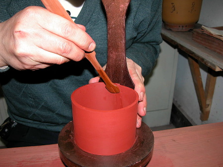 22、用“拍子”顶住身筒黏合处的外围，再用“小竹插”的后部来修刮整平身筒的黏合处。